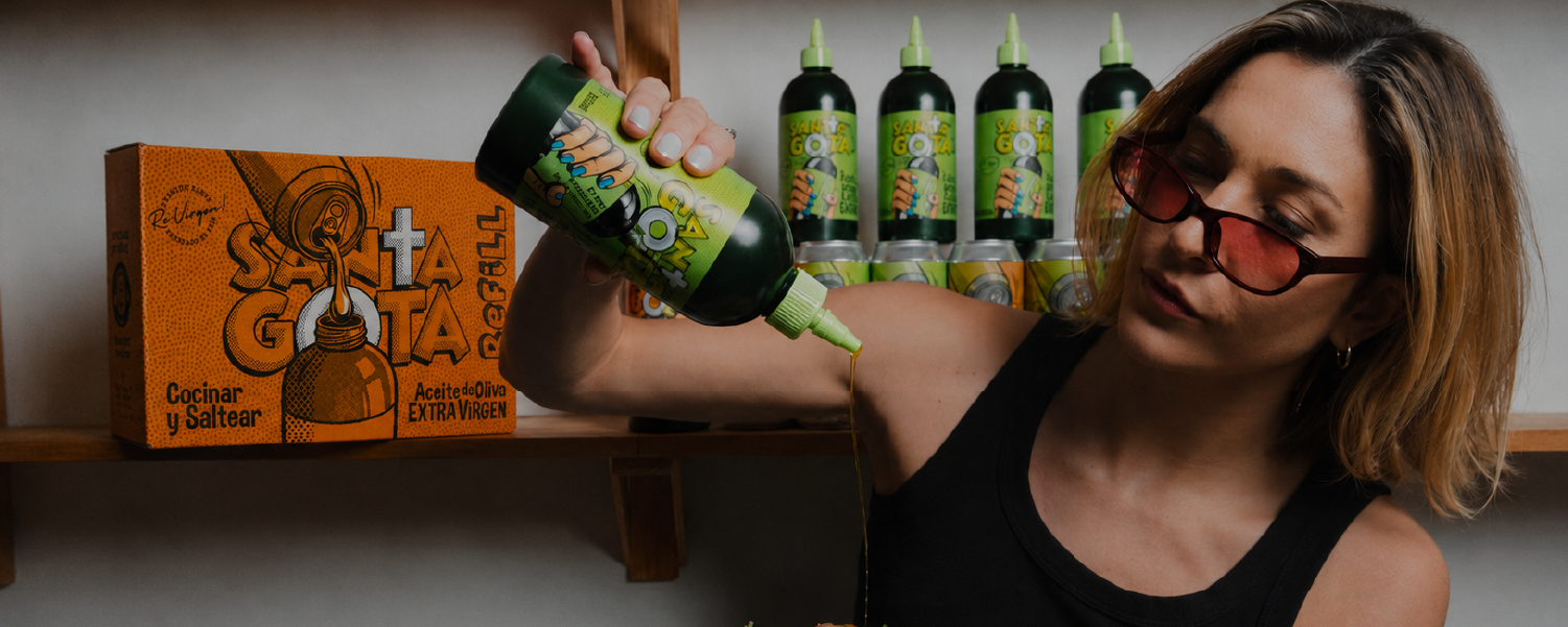 Mujer sirviendo aceite de oliva desde un squeeze Santa Gota junto a una caja refill naranja y botellas en un estante