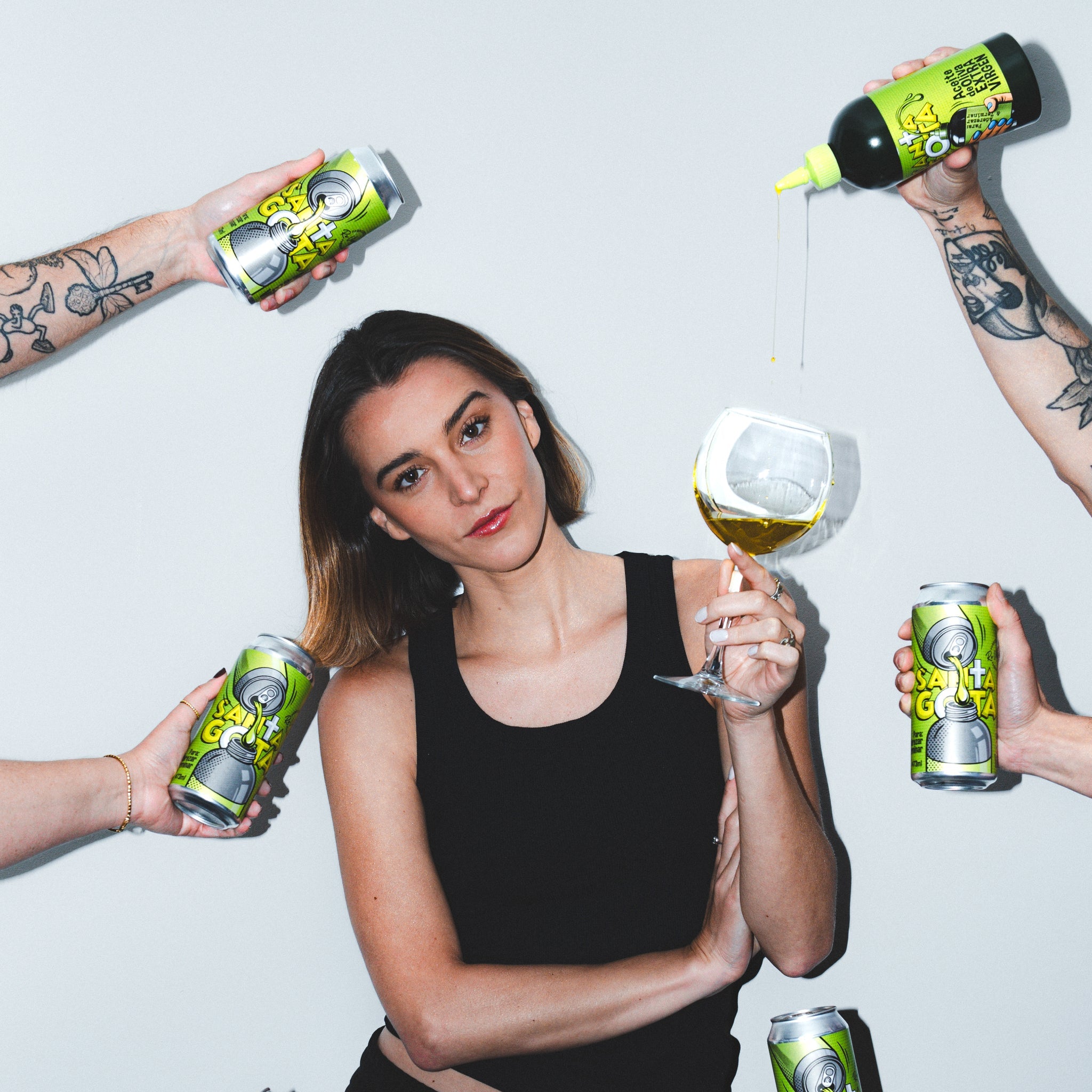 Mujer con una copa de aceite de oliva rodeada de manos que sostienen latas y squeeze de Santa Gota